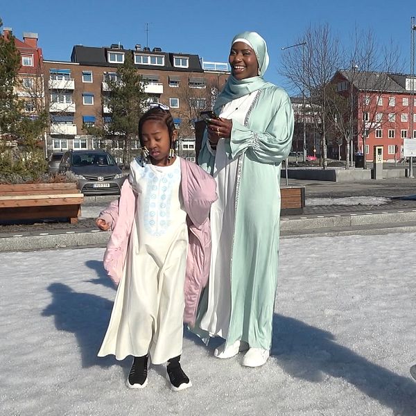 Familj på en snötäckt plats, barn med rosa ballong. Solig dag i ett bostadsområde.