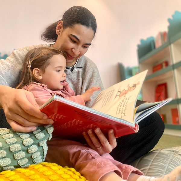 Mamma Sandy Heijbel sitter och läser en bok på biblioteket med Amacia 3 år.