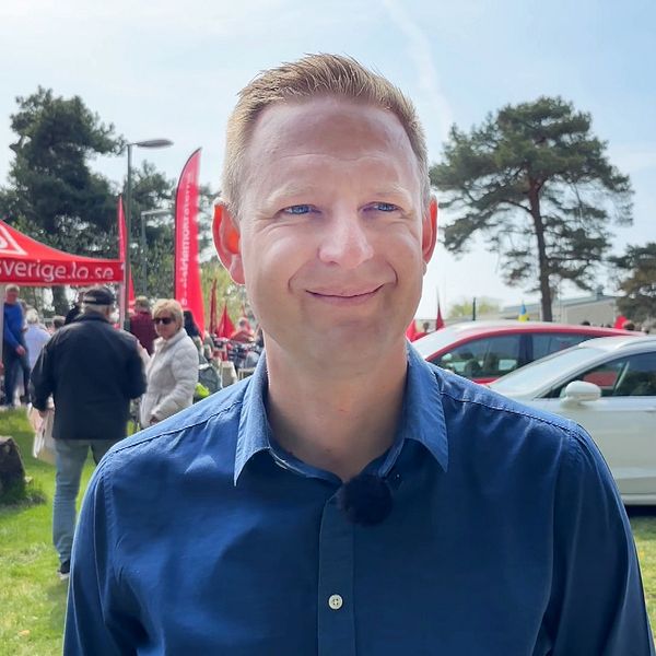 Per Svensson (S) bär blå skjorta och står utomhus vid ett evenemang med folk, tält och bilar i bakgrunden.