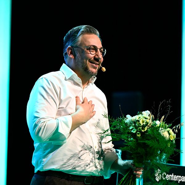 Muharrem Demirok i vit skjorta talar på Centerpartiets scen och håller en blombukett.