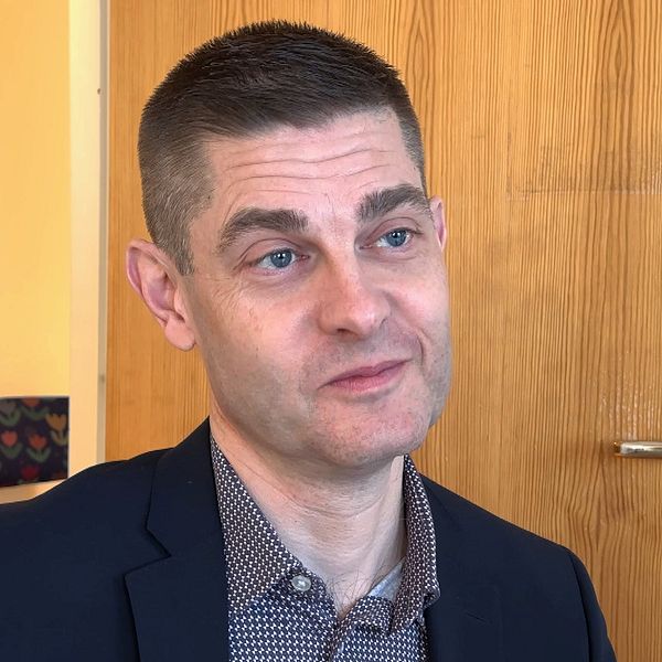 En man med kavaj sitter inomhus framför en trädörr.