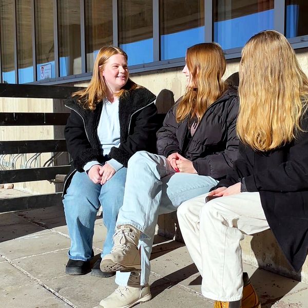 tre unga tjejer sitter på en bänk utomhus.