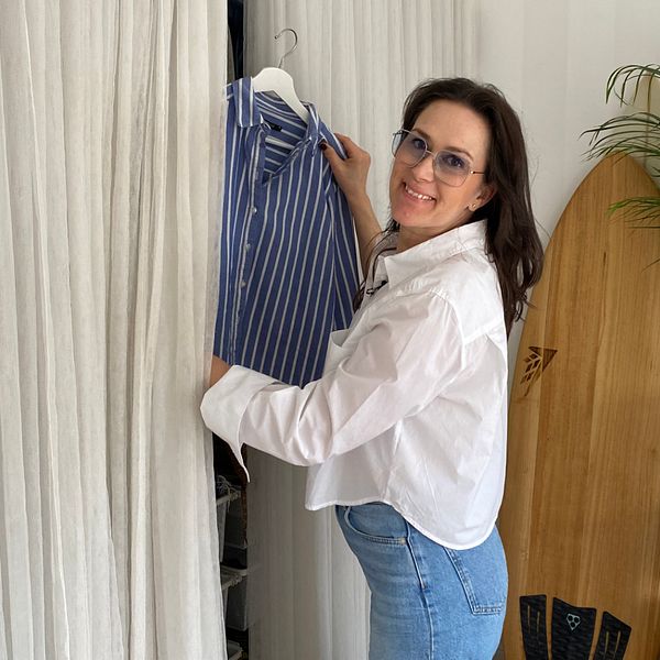 Bild på kvinna i jeans och vit skjorta som lyfter ut en randig skjorta på en galge från en garderob.