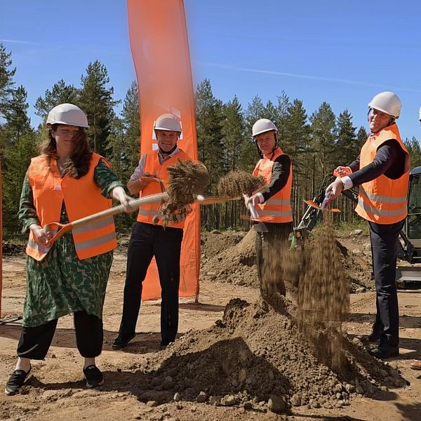 fem personer i orange västar och vita hjälmar, fyra av dem tar ett spadtag