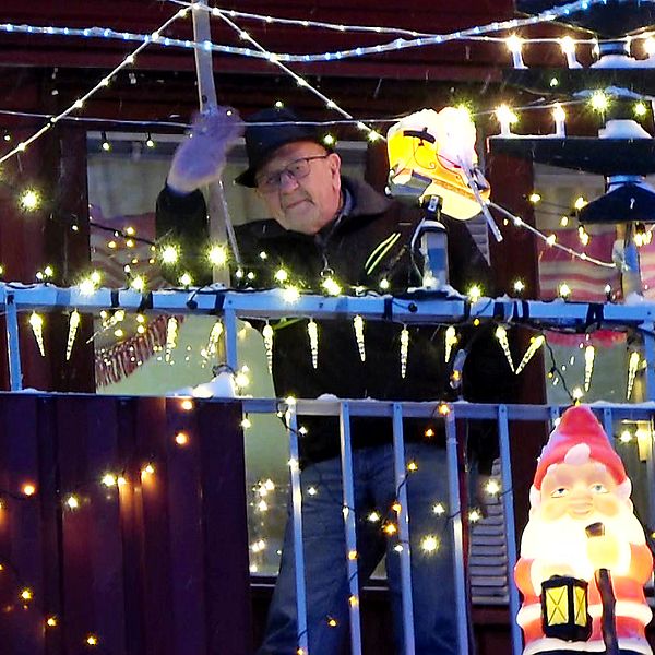 84-årige Donald Johansson i Arvidsjaur står och vinkar på sin julpyntade balkong