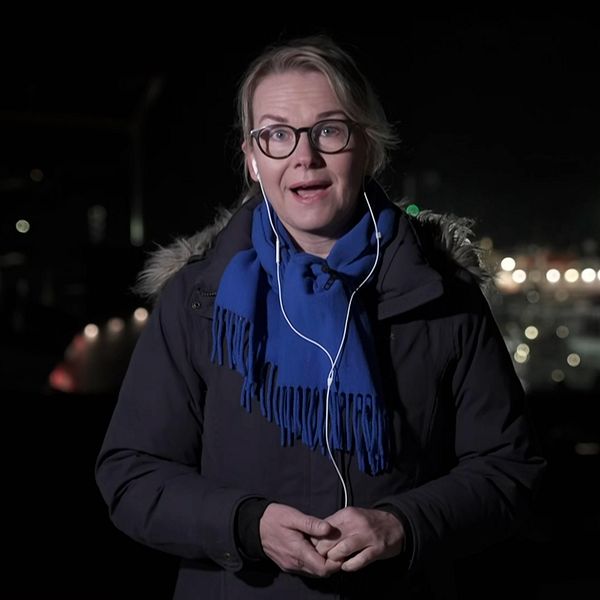 Person i mörk jacka och blå halsduk med nattlig stadsmiljö i bakgrunden.