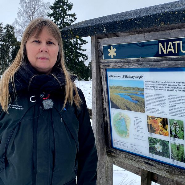 Eva Wallander, enhetschef naturvårdsförvaltningen länstyrelsens jönköping, kvinna med ljust hår och blå jacka står vid en naturreservatsskylt vid Barkerydssjön