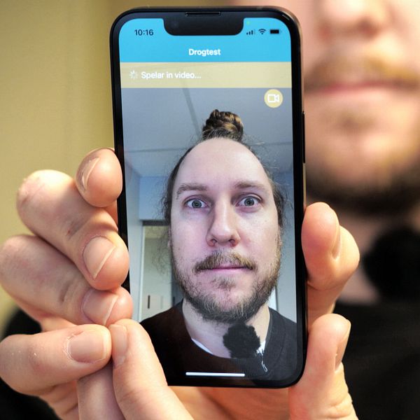 Man håller en mobil med en bild på sig själv