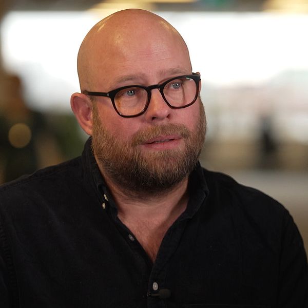 Fotograf Anders Hansson sitter i en korridor, klädd i en mörk skjorta. Bakgrunden är oskarp.
