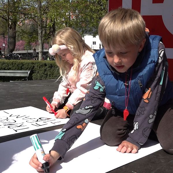 Två barn ritar med tuschpennor på stora vita papper utomhus vid evenemang.