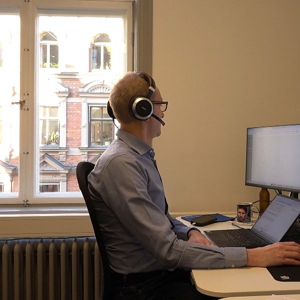 en man sitter med ett headset framför tre dataskärmar
