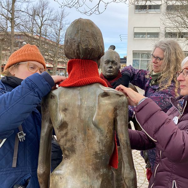 Kvinnor knyter röda halsdukar runt statyer