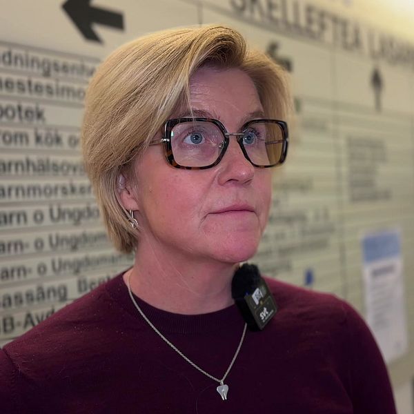 Kvinna med glasögon står framför en skylt inne på Skellefteå lasarett.