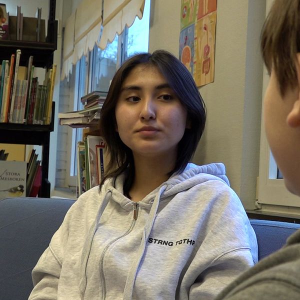 Två elever sitter i en soffa, en har ryggen mot kameran. De sitter bredvid en bokhylla.