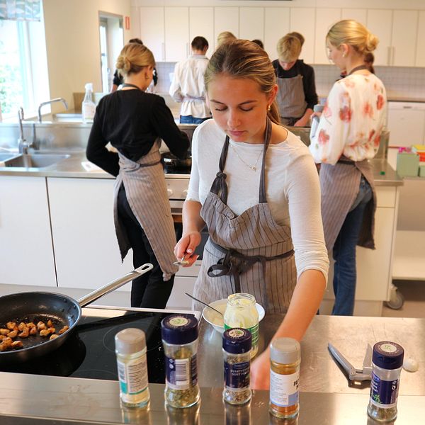 Ungdomar lagar mat tillsammans i ett skolkök, flera kryddburkar syns på bänken.