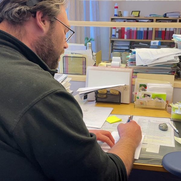 En man sitter på ett kontor och skriver på papper med en analog miniräknare vid sin sida.
