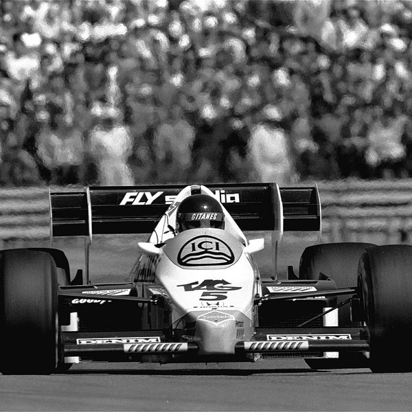 Två formelbilar tävlar på bana, publik syns i bakgrunden.