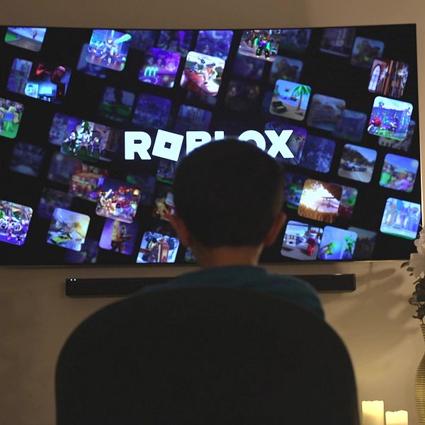 Ett barn sitter framför en stor TV som visar en mängd olika miniatyrbilder från spelet Roblox.