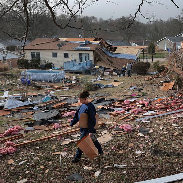 Man går genom förödelse av förstörda hus efter en tornado i en bostadsområde.