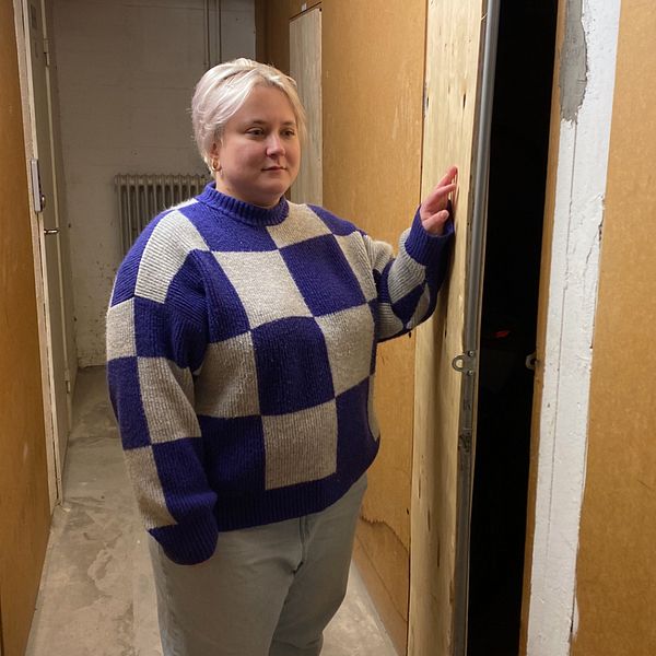 Kvinna står i rutig stickad tröja i en korridor mellan lägenhetsförråd.
