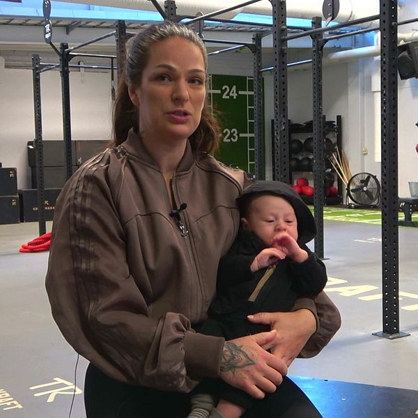 En kvinna sitter på ett gym och håller i en bebis i famnen