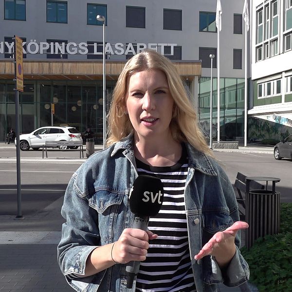 SVT:s reporter Frida Grunnvald står utanför Nyköpings lasarett med en mikrofon och är vänd mot kameran.