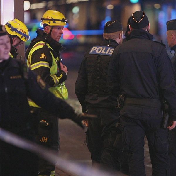 Poliser och brandmän utanför den brandhärjade byggnaden. Det är mörkt ute och i bakgrunden syns blåljus