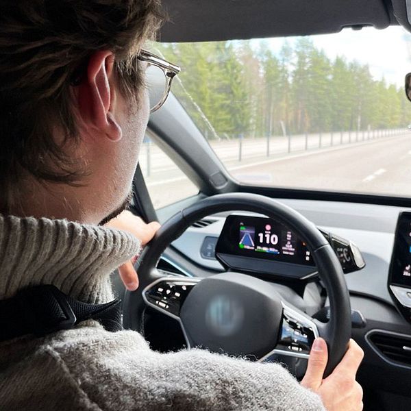 En person kör bil på landsväg med digitala skärmar som visar bilens navigation.
