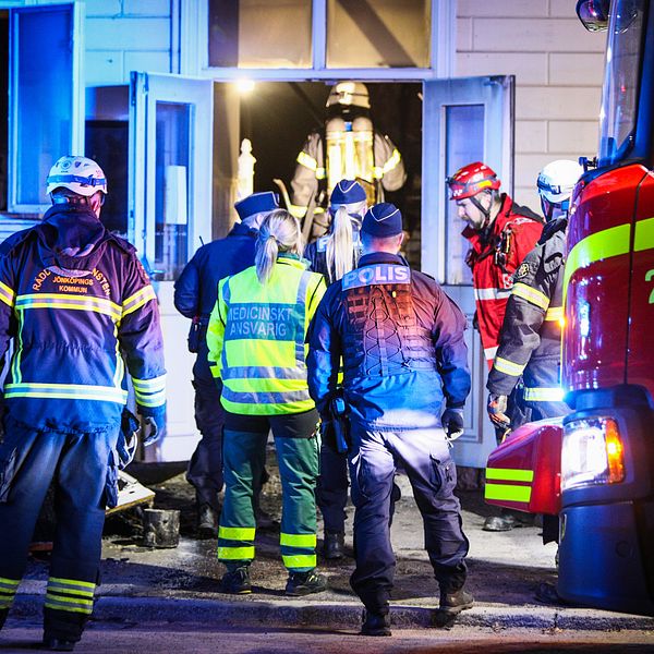 Brandmän och räddningspersonal arbetar vid ett hus, en brandbil står i förgrunden.