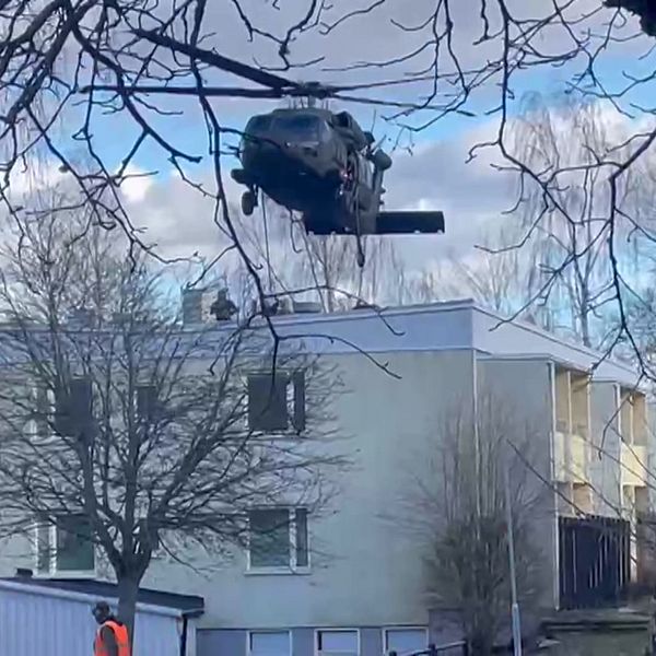 Militärhelikopter hovrar ovanför ett hus medan personer hissar ner sig på hustaket.