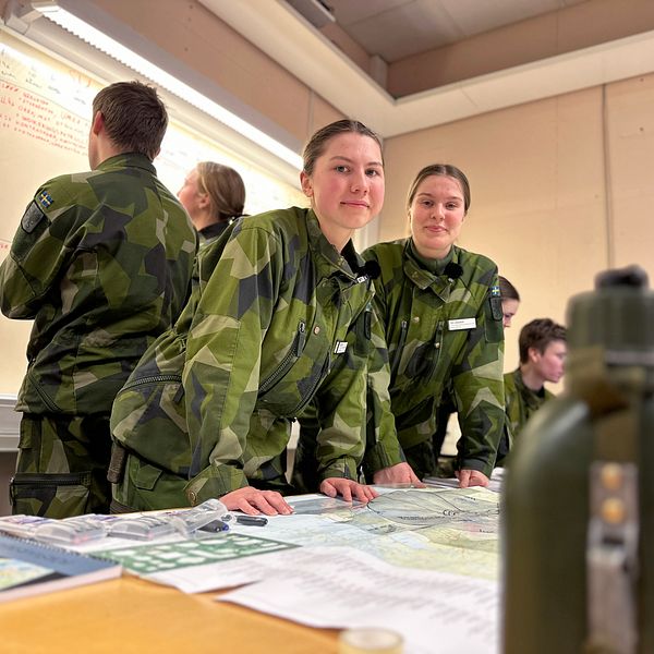 Värnpliktiga Moa Snitting Olcén och Ida Lindgren på Skydd C i Umeå lutar mot ett bord med en karta