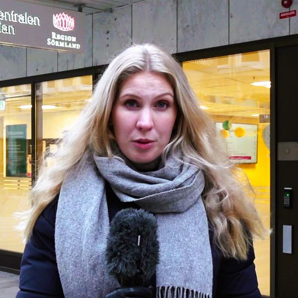 Reporter Frida Gunnvald står framför Vårdcentralen Gallerian med en mikrofon i handen.