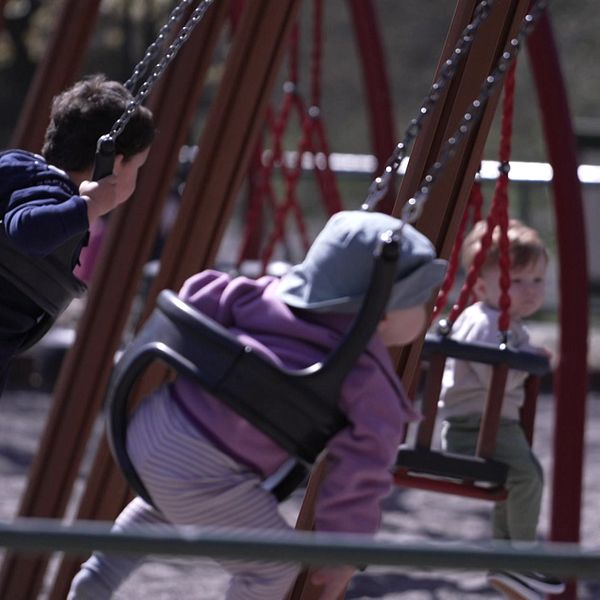 Tre unga barn gungar i en lekpark.