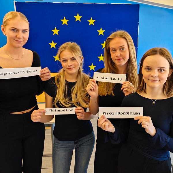 Fyra tjejer i 17-18-årsåldern står vid en EU-flagga i ett klassrum