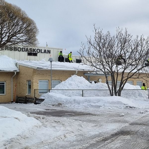 personer i varselkläder syns på taket på Östra Ersbodaskolan, snöhögar nedanför