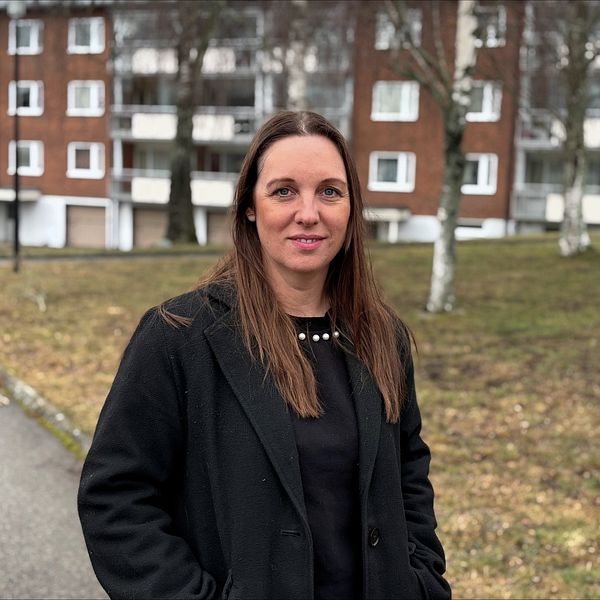 Person står utomhus framför tegelhus och grönområde.