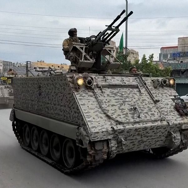 Militära fordon åker längs en gata, där en soldat på en kulspruteposition syns på toppen av fordonet.