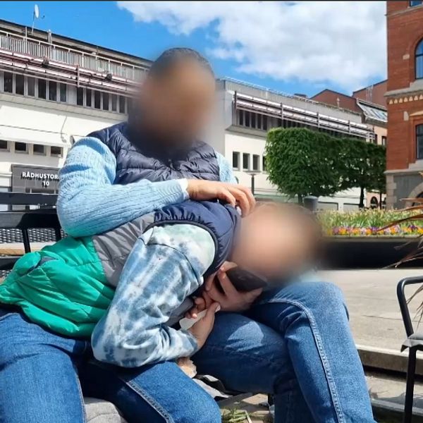 Två personer sitter nära varandra utomhus på en bänk med oskarpa ansikten.