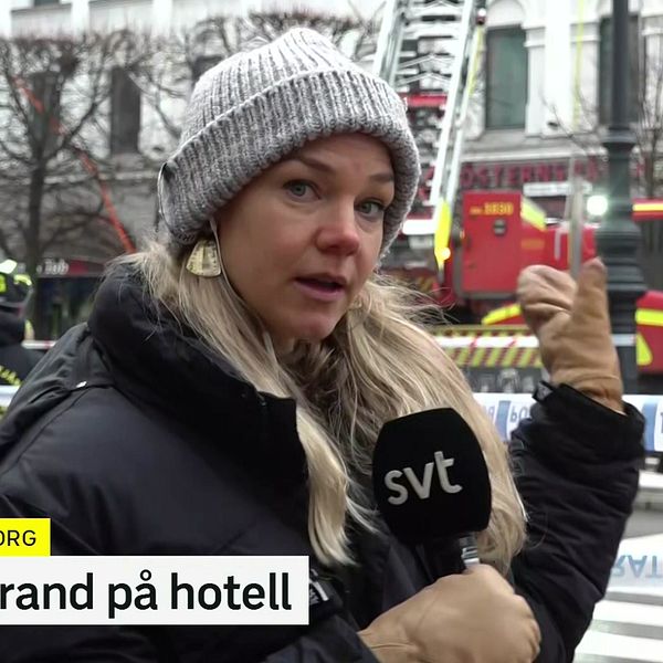 En reporter står i förgrunden och rapporterar om en storbrand på ett hotell i Helsingborg, med brandbilar och räddningstjänst synliga i bakgrunden. Trafikljus och avspärrningar är också synliga, vilket indikerar att området är stängt för allmänheten. Texten ”Storbrand på hotell” ingår i bilden.