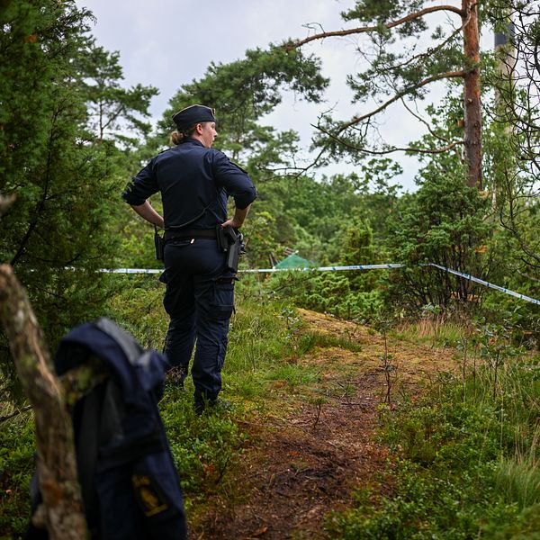 Poliskvinna står i en skogsglänta.