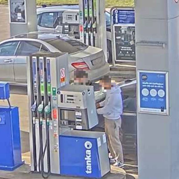 Två män tankar sin bil vid en bensinstation, fler bilar syns i bakgrunden.