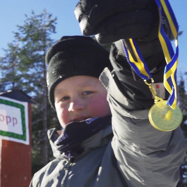 En liten pojke håller upp en medalj framför kameran som han vann i barnens vasalopp.