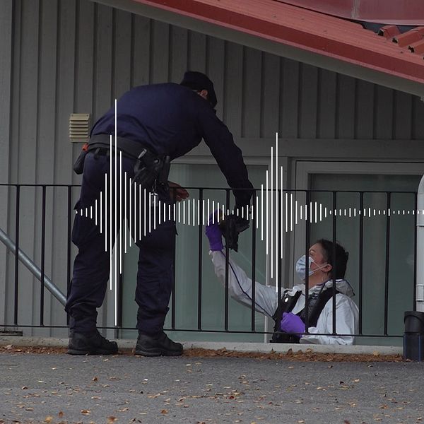 En uniformerad polis och en person i vit rock och lila plasthandskar utbyter ett föremål.