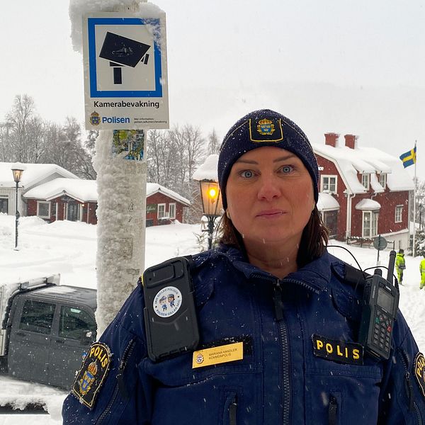 Kommunpolisen Mariana Handler står i Åre med Åre torg i bakgrunden. En skylt som indikerar kameraövervakning sitter på en stolpe. ä