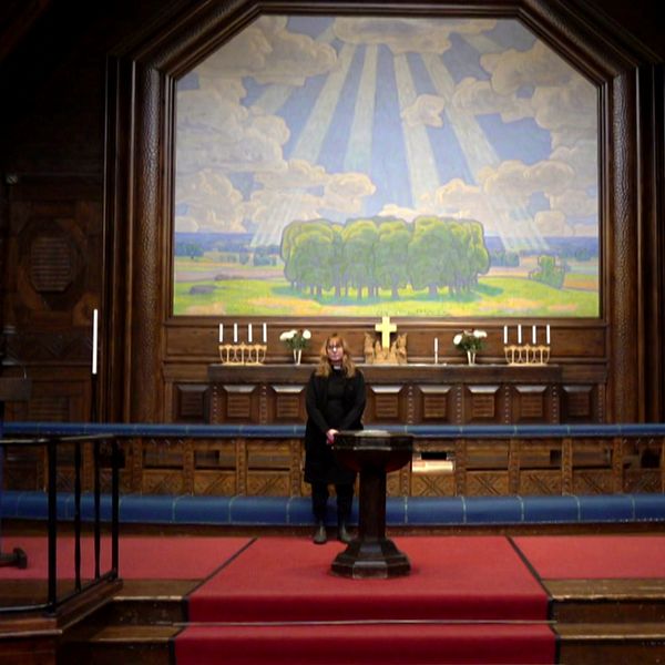 Kyrkoherden Lena Tjärnberg står framför Prins Eugens altartavla i Kiruna kyrka.