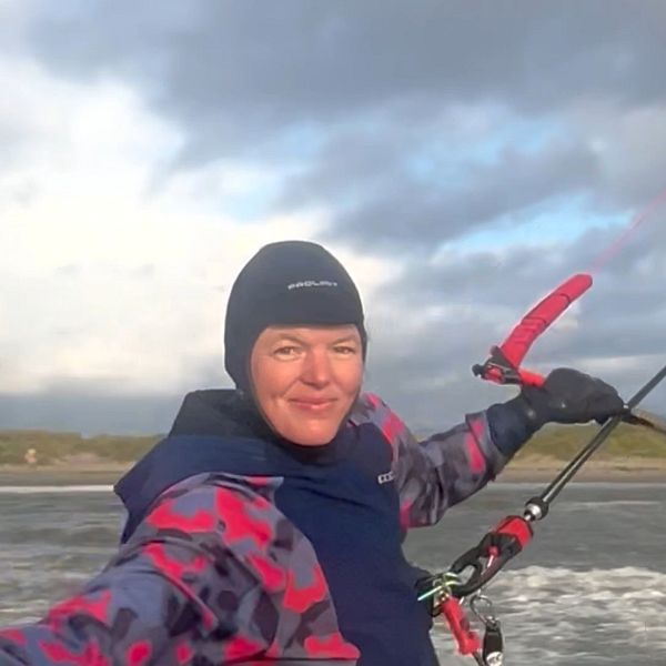 Person i färgglad jacka kitesurfar vid en stormig kust under molnig himmel.
