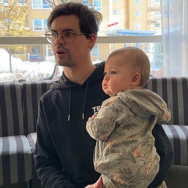 En man med glasögon sitter på golvet med ett barn i knäet.
