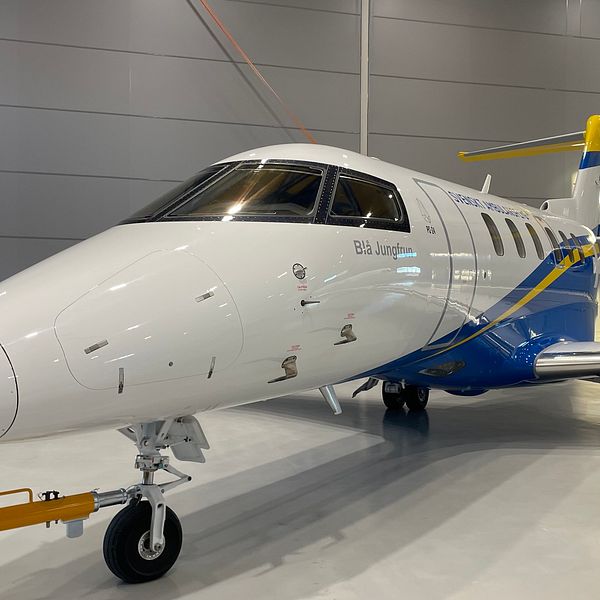Ett av Svenskt Ambulansflygs flygplan i en hangar. Planet är vitt med blå och gula detaljer.