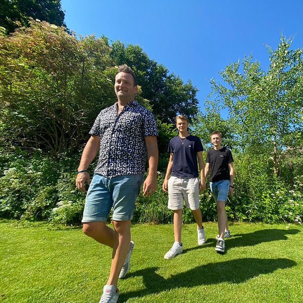 Tre bandmedlemmar från dansbandet Donnez går över en gräsmatta en solig sommardag.