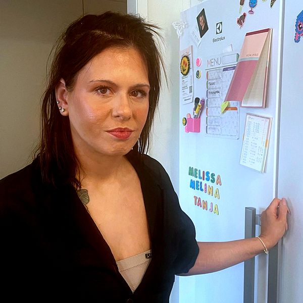 Person vid kylskåp, prydd med magnetiska lappar och teckningar.